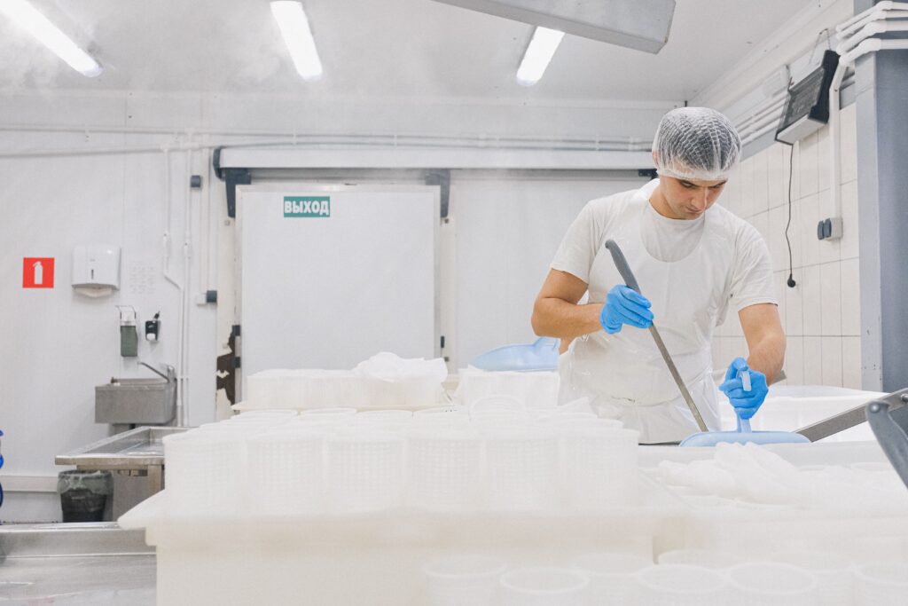 Un homme dans une usine agroalimentaire travaille. Il porte un équipement dont une charlotte sur les cheveux, des gants et un tablier en plastique.
